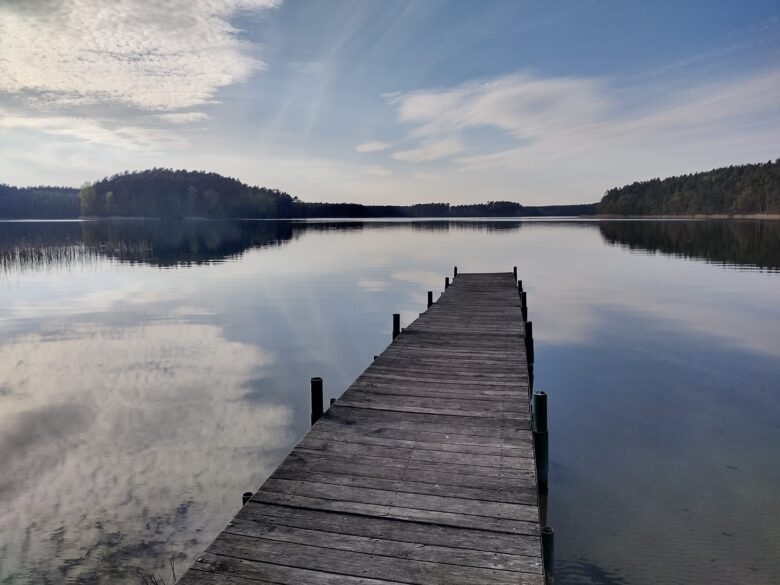 Zdjęcie przedstawia pomost na jeiorze Sosno i odbicie nieba w tafli jeziora.